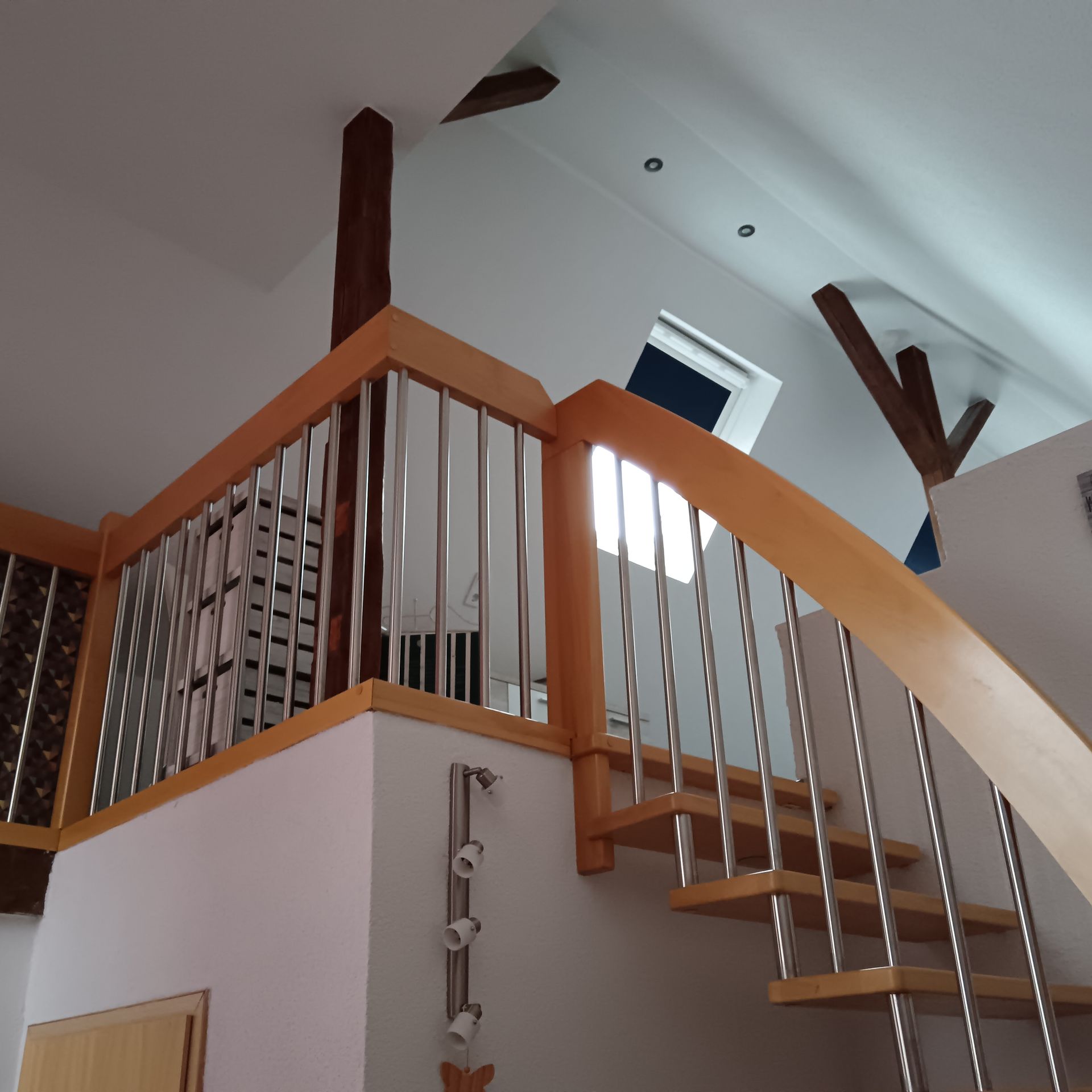 Holztreppe mit Metallgeländer, helles Holz und weiße Wände.