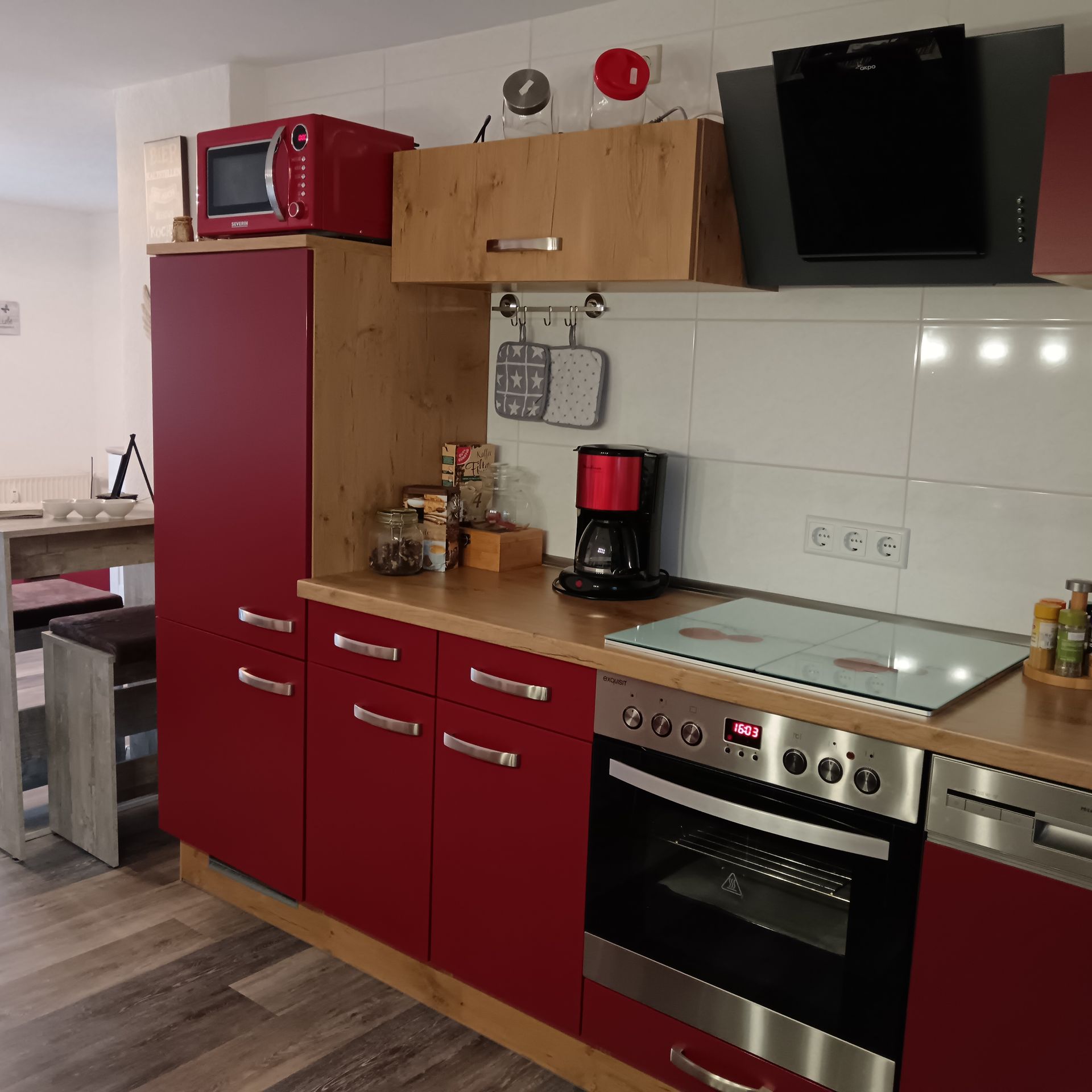 Küchenschränke in Rot- und Holztönen mit Mikrowelle, Backofen, Kochfeld und Kaffeemaschine.