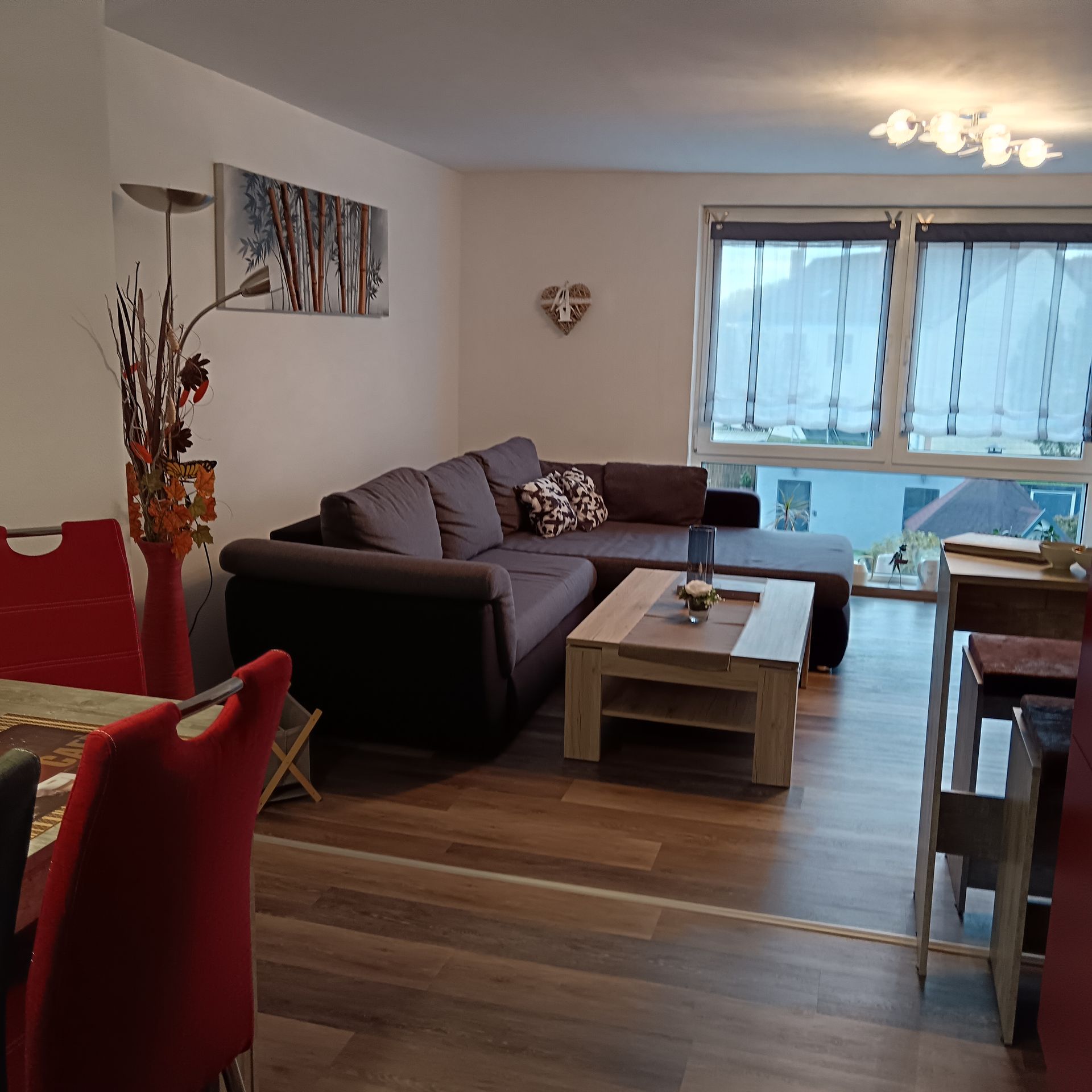 Wohnzimmer mit ausziehbarem Ecksofa, Couchtisch und Esstisch mit roten Stühlen.