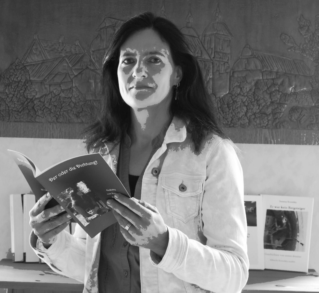 Susanne Kowalsky mit schwarzen Haaren und ohne Brille. Sie sieht in die Kamera und hält dabei ein aufgeschlagenes Buch in den Händen.