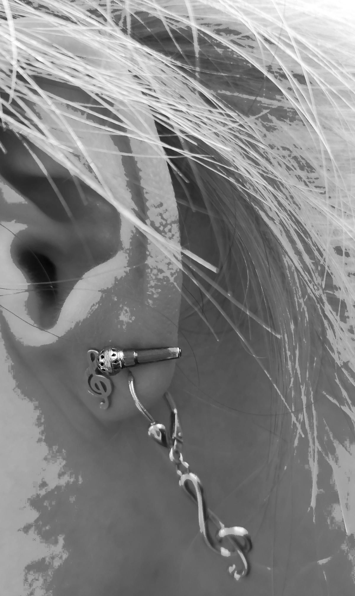 Linkes Ohr mit 3 Ohrringen, davon 1 Noteschlüssel als Stecker, einer als Hänger und einem Mikrofon als Stecker.