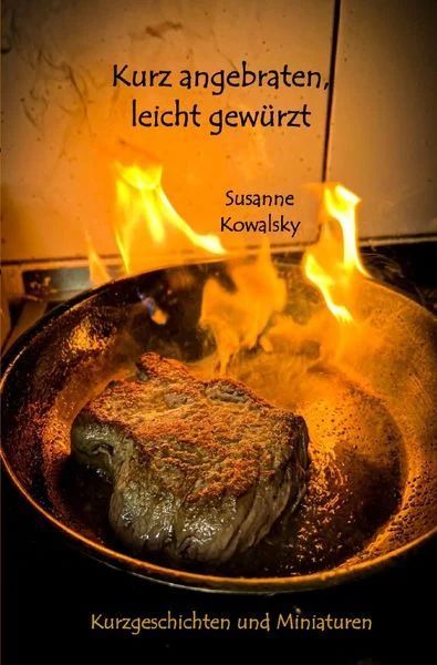 Eine Pfanne auf dunkelorangem Untergrund. Ein Steak bruzzelt in der Pfanne. Es sind Flammen erkennbar.