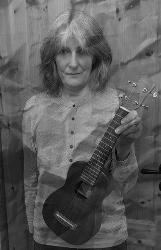 Eine Frau sieht in die Kamera. Sie hält eine Ukulele in der Hand.