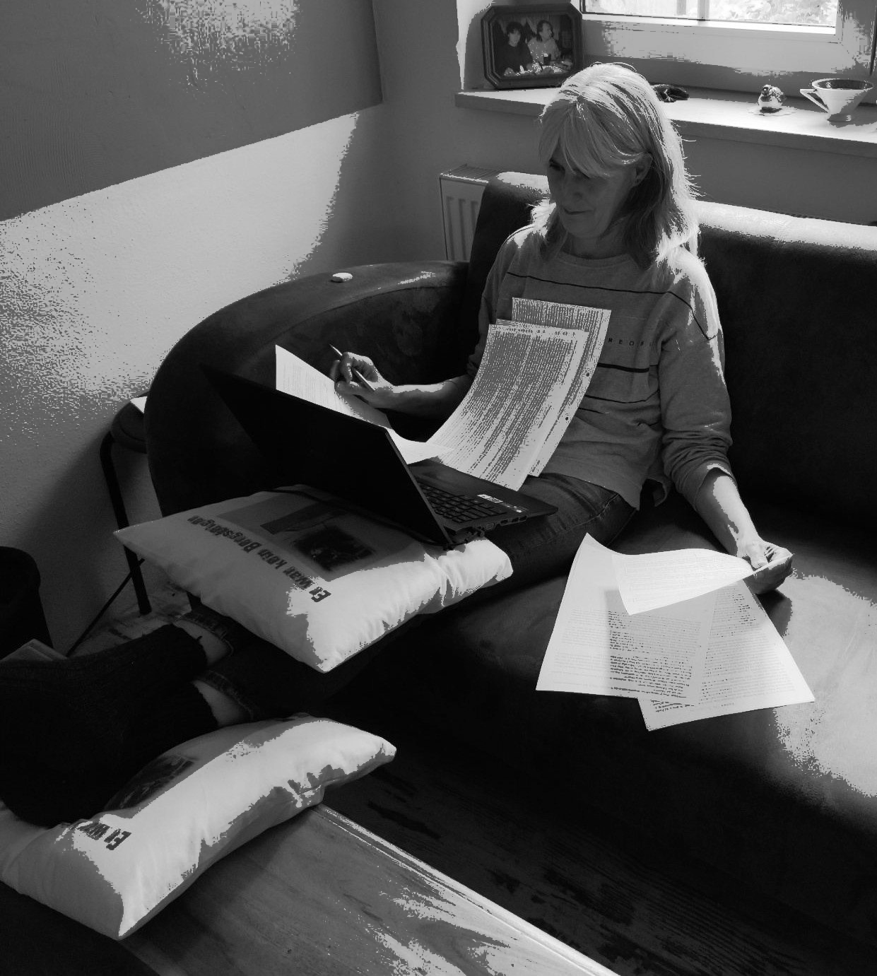 Susanne Kowalsky beim Schreiben Susanne Kowalsky sitzt auf einer Couch, die Füße ausgestreckt auf dem Tisch, inmitten von Zetteln und einem Laptop.