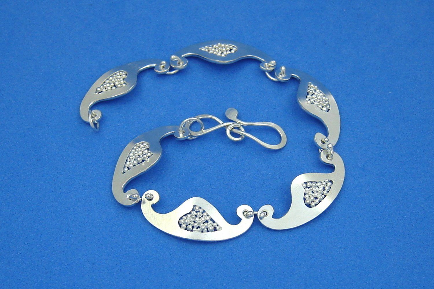 schmales gegliedertes Armband aus Argentium-Sterlingsilber mit Gliedern in Form kleiner Schiffchen, deren zentraler Ausschnitt mit kleinen Silberkügelchen gefüllt ist, geschlossen mit einer schleifenförmigen Drahtschließe