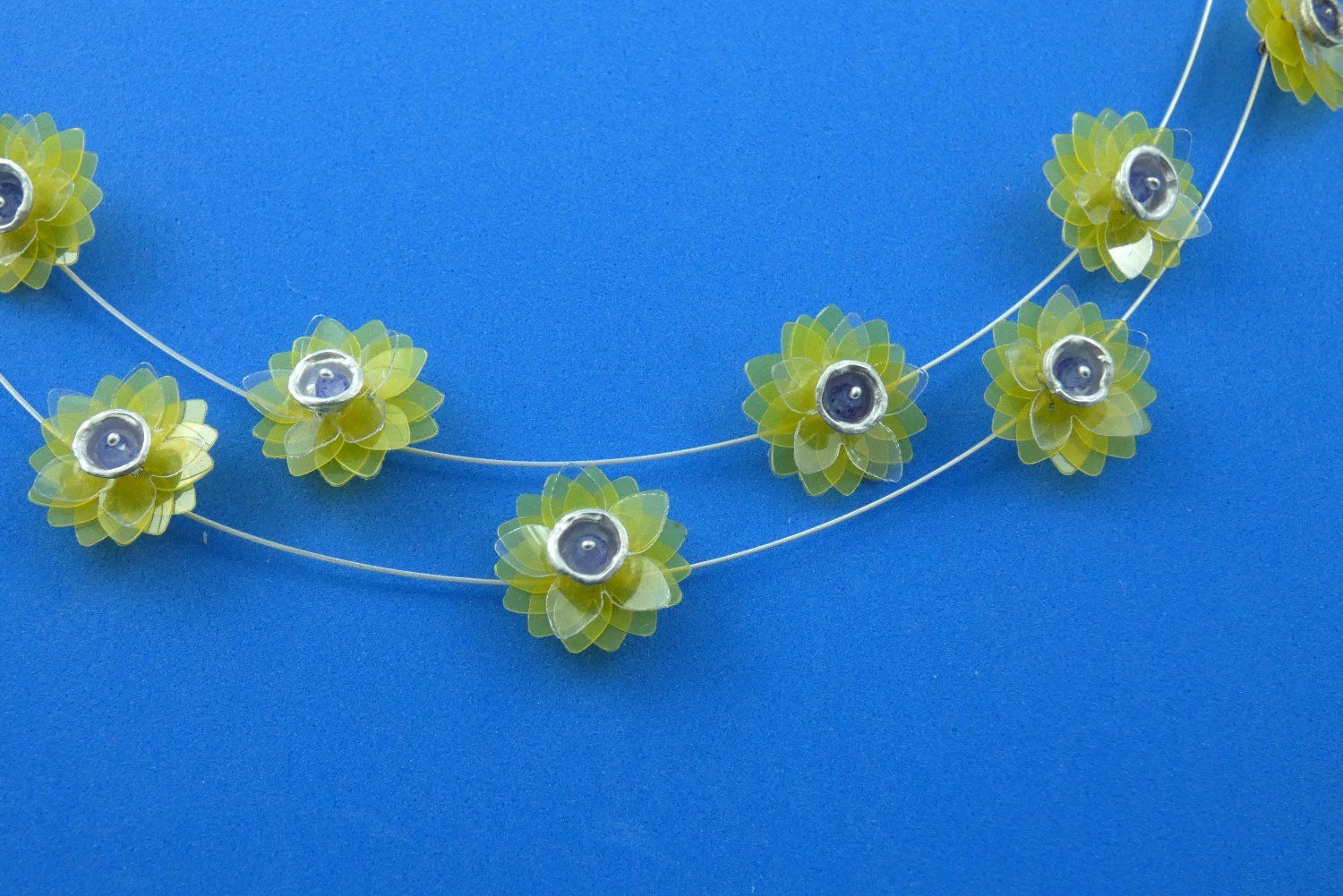 Stahlseide-Collier mit kleinen gelben transparenten Büten, die im Zentrum ein Becherchen aus Argentium-Sterlingsilber tragen, das mit einer himmelblauen Tansanit-Perle gefüllt ist