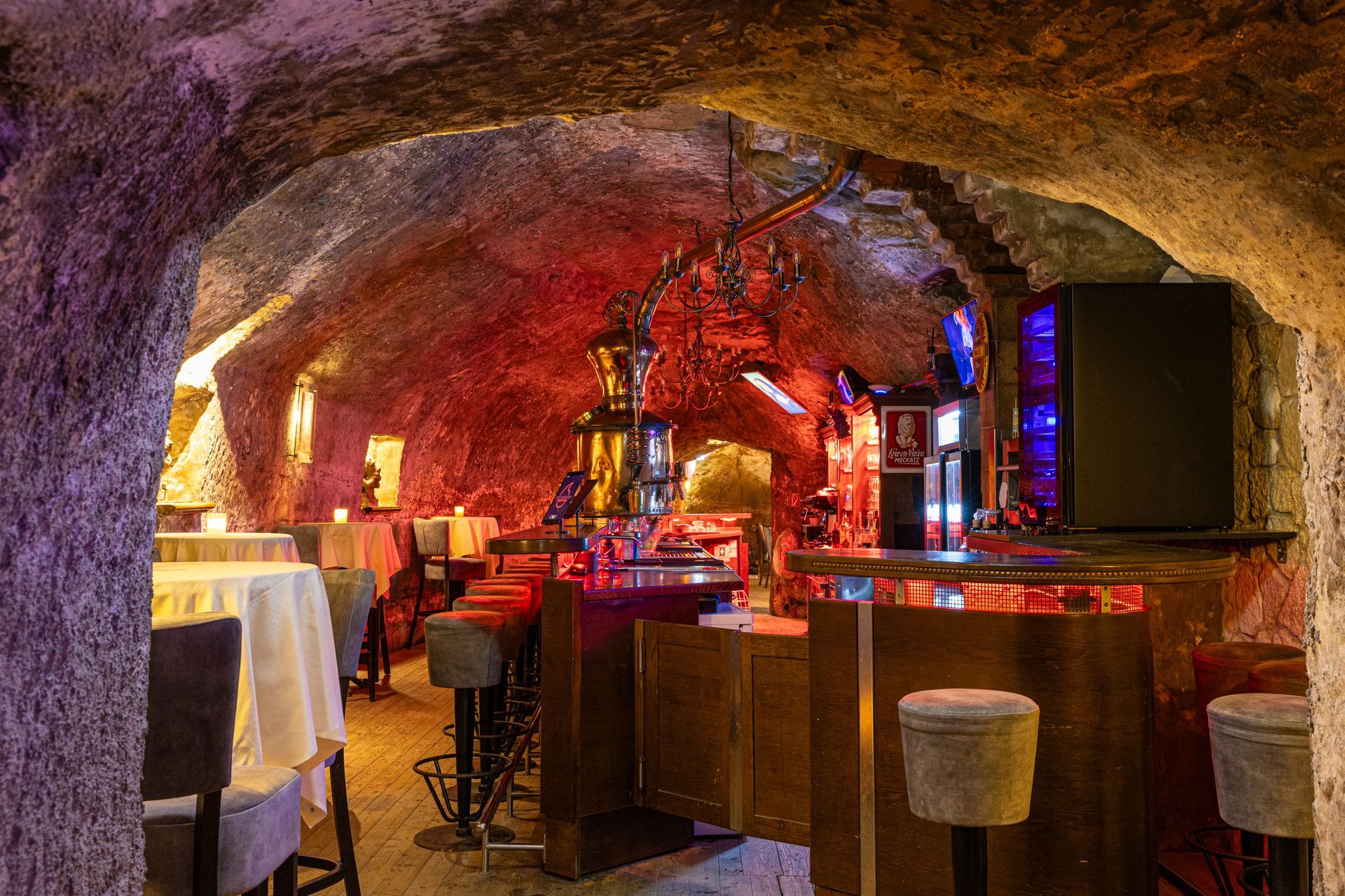 Gemütliche Bar im Höhlenstil mit roter Beleuchtung, Holzhockern und leuchtenden Flaschen und Dekorationen
