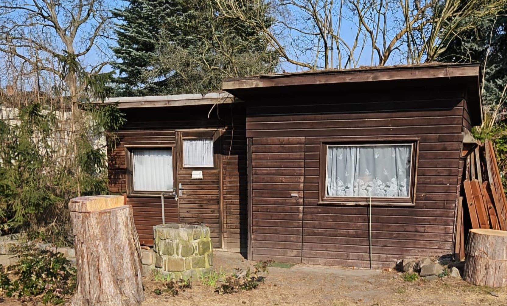 Gartenlaube mit brauner Holzverkleidung und zwei unterschiedlich hohen Dachbereichen.