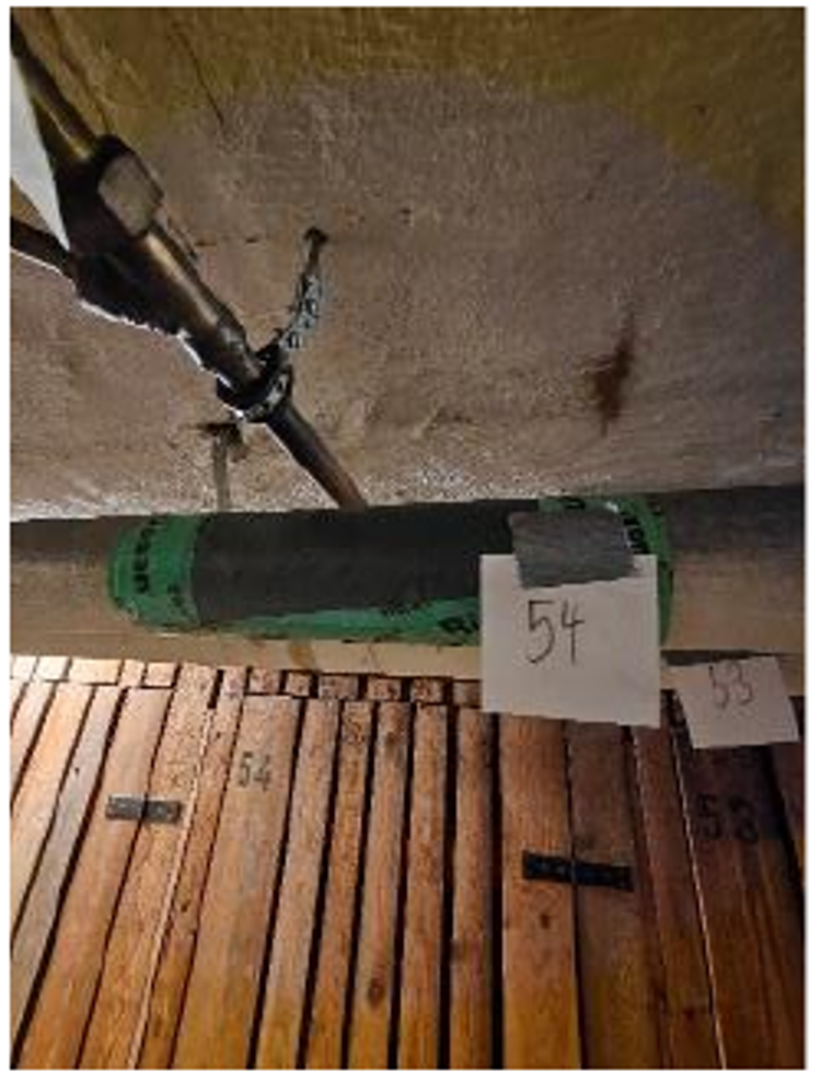 Örtlich gesicherte Rohrummantelung mit Markierung 54 unter einer Kellerdecke.