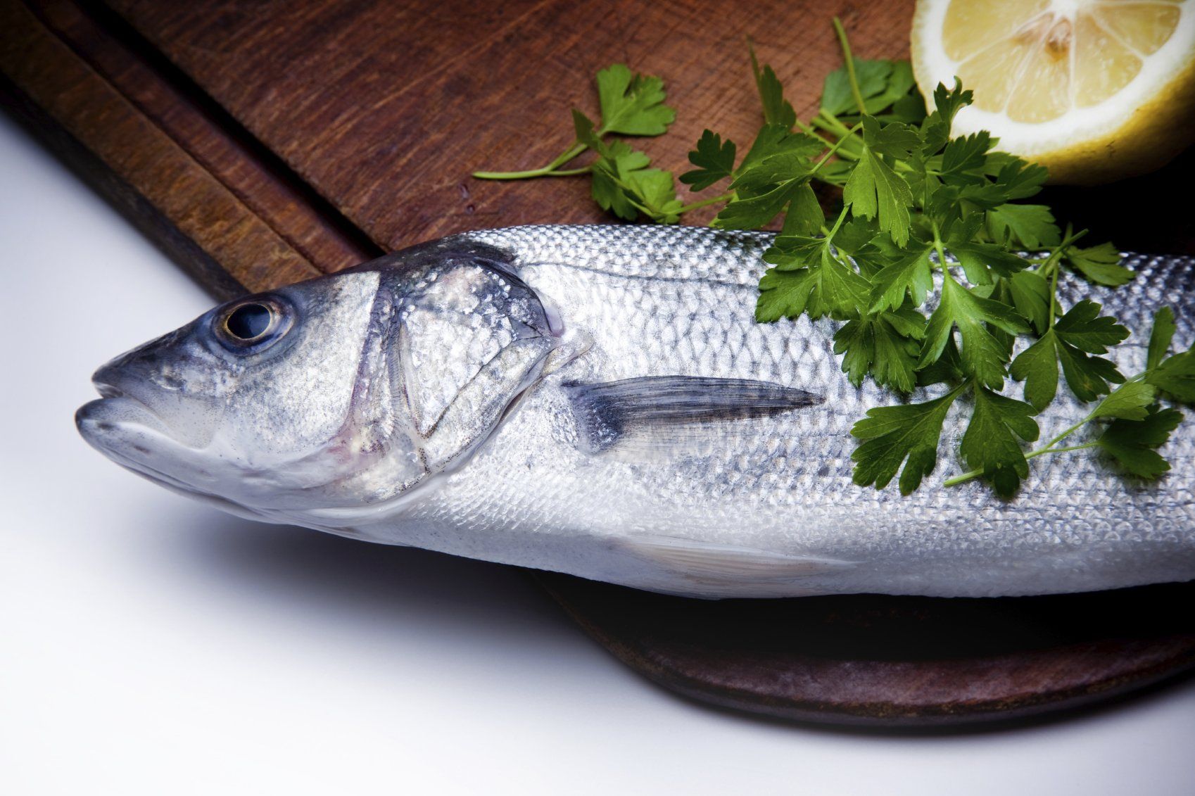 Es liegt ein toter Fisch auf einem Schneidbrett. Der Fisch ist von Gartenkräutern bedeckt. 