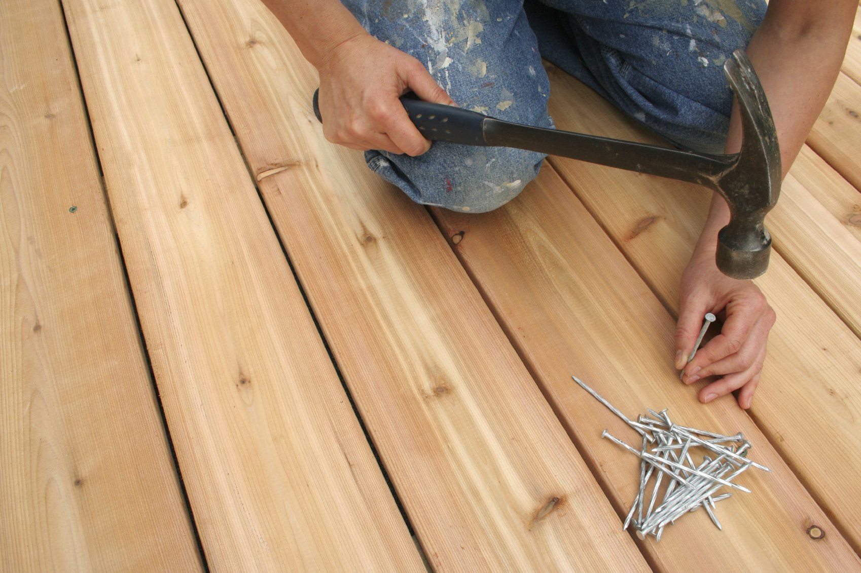 A woodworker hammering a nail into an outside deck