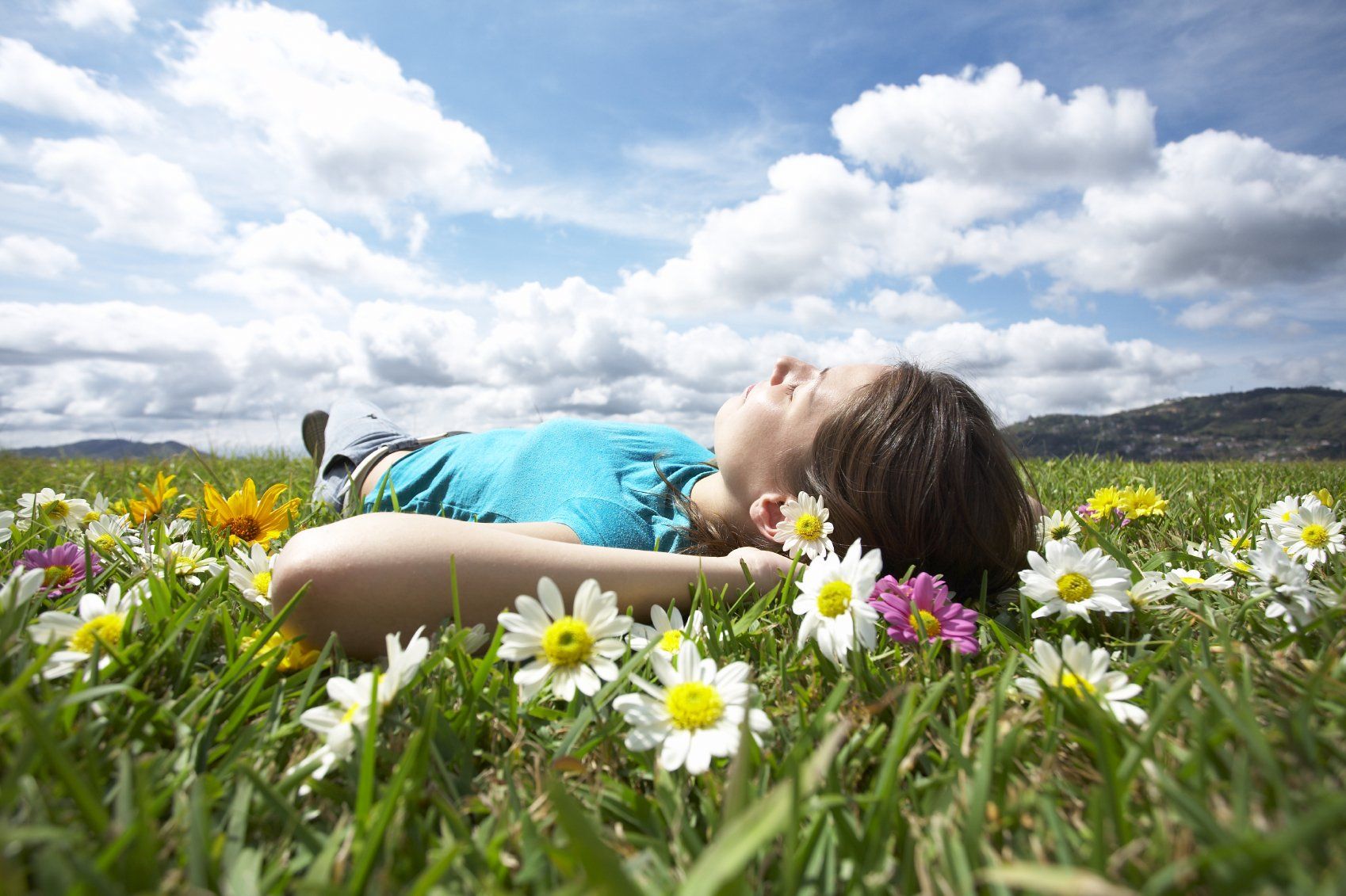Eine Frau liegt entspannt auf einer Blumenwiese unter einem sonnigen Himmel