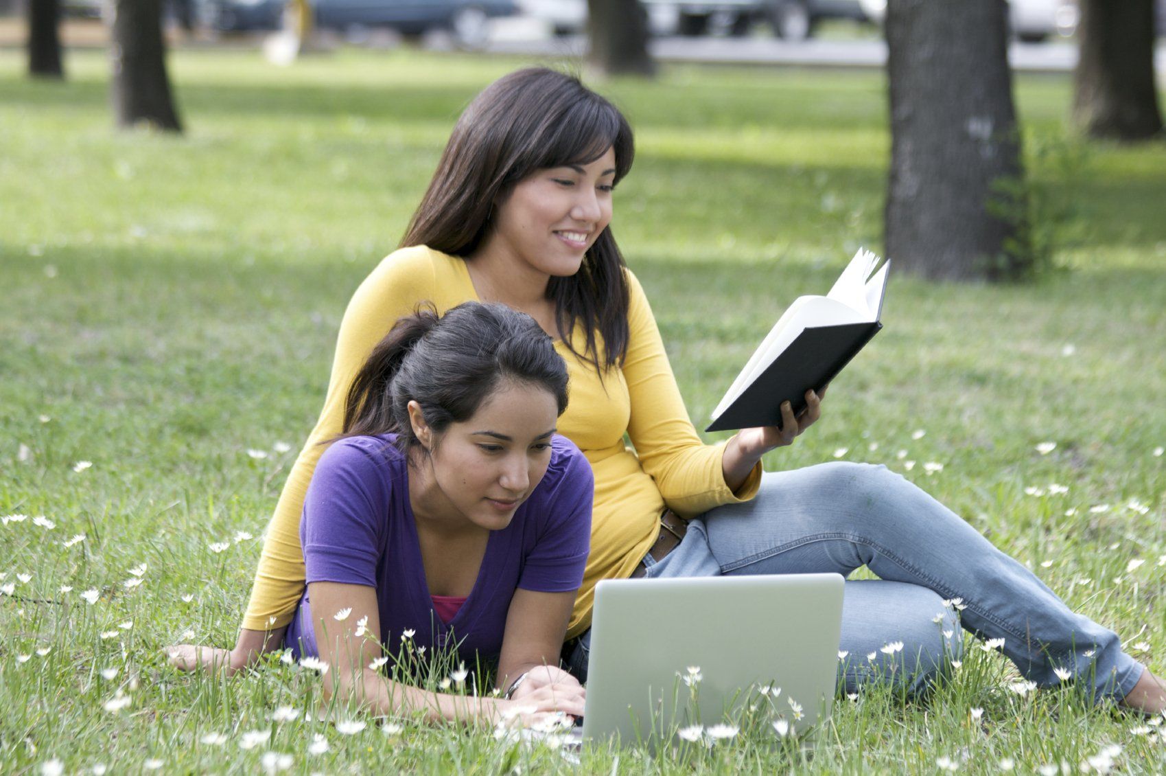 Two young ladies lying on the grass, reading.