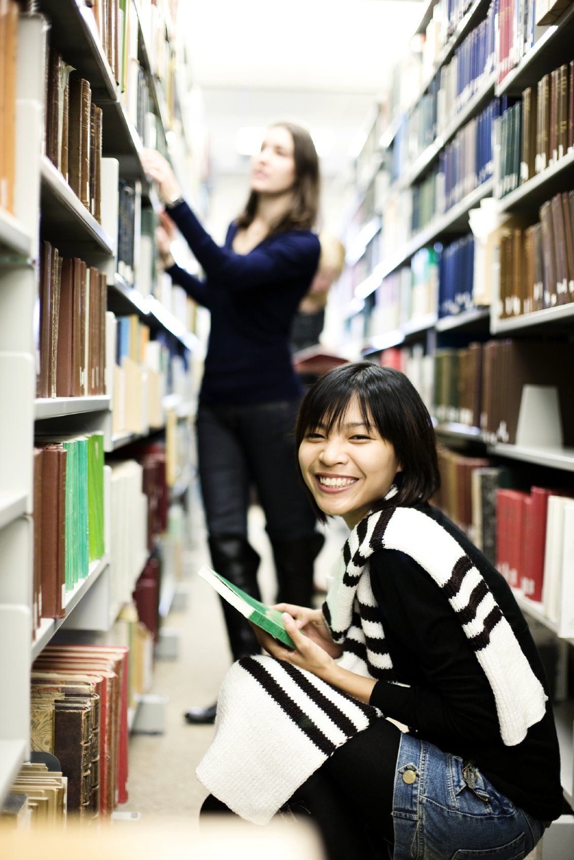 Two young ladies searching for books in a library.