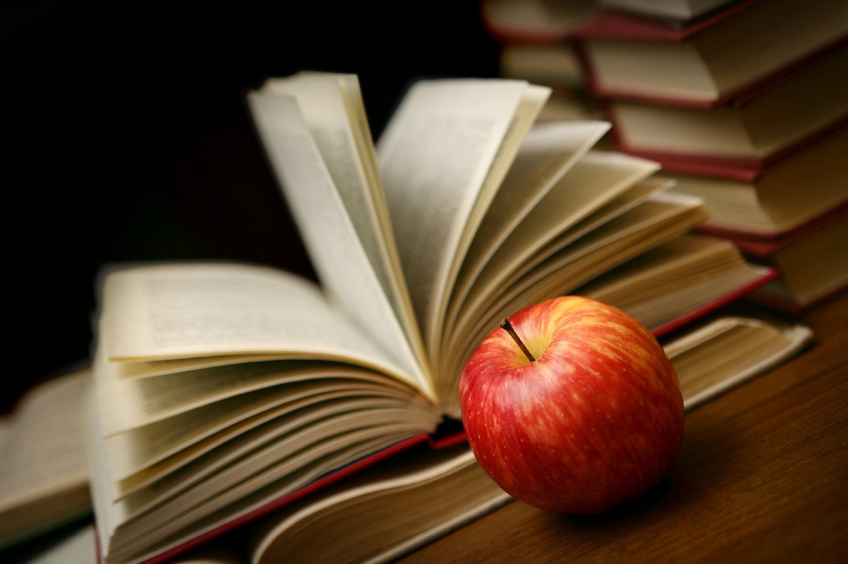 Lifelong Learning. Open book on desk, next to a red apple