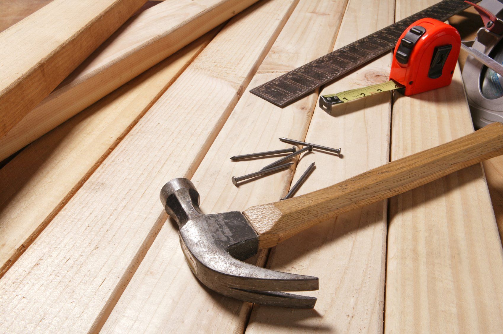 A hammer, nails and measuring tools sitting on a workbench.