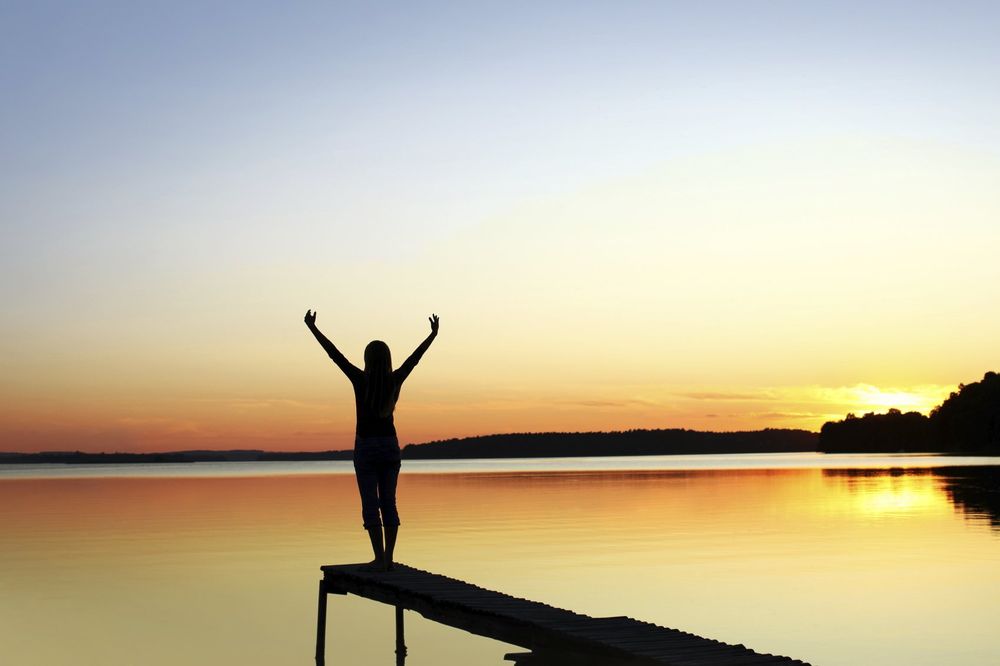 Person standing on dock stretching at sunset