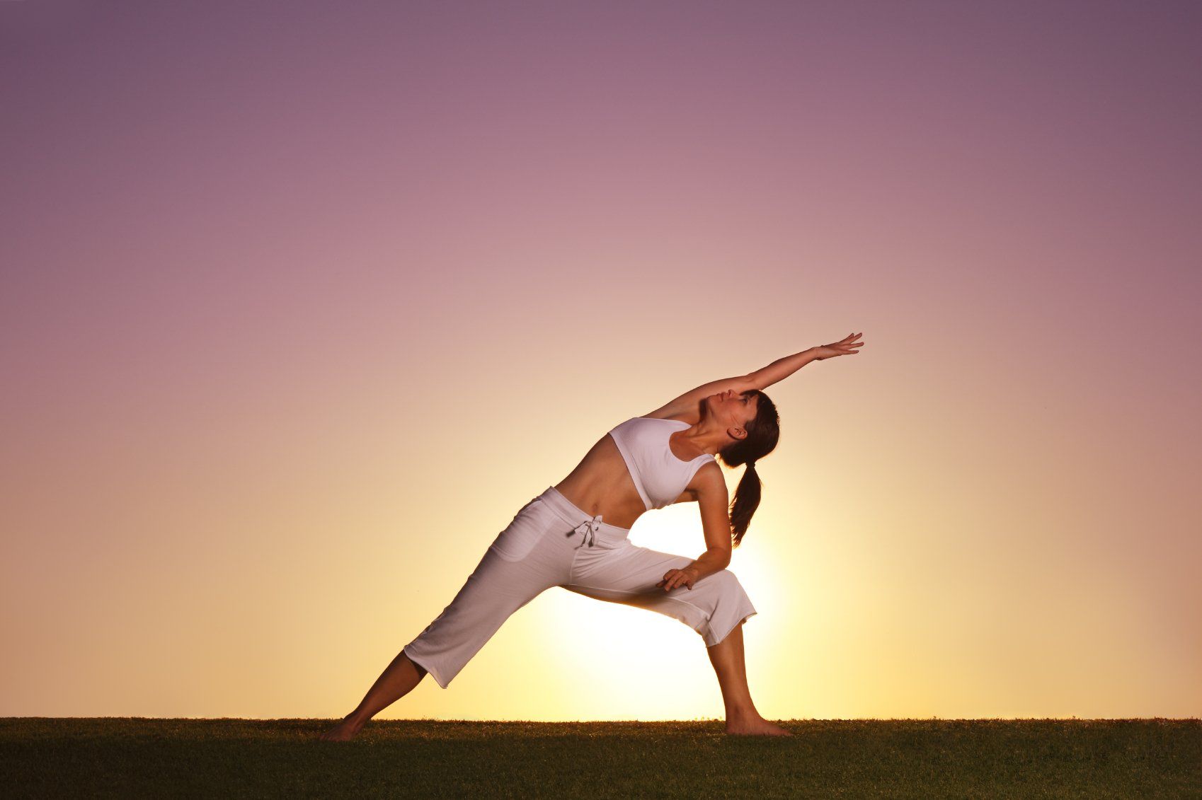 woman doing yoga with arm stretched upwards and sun behind her