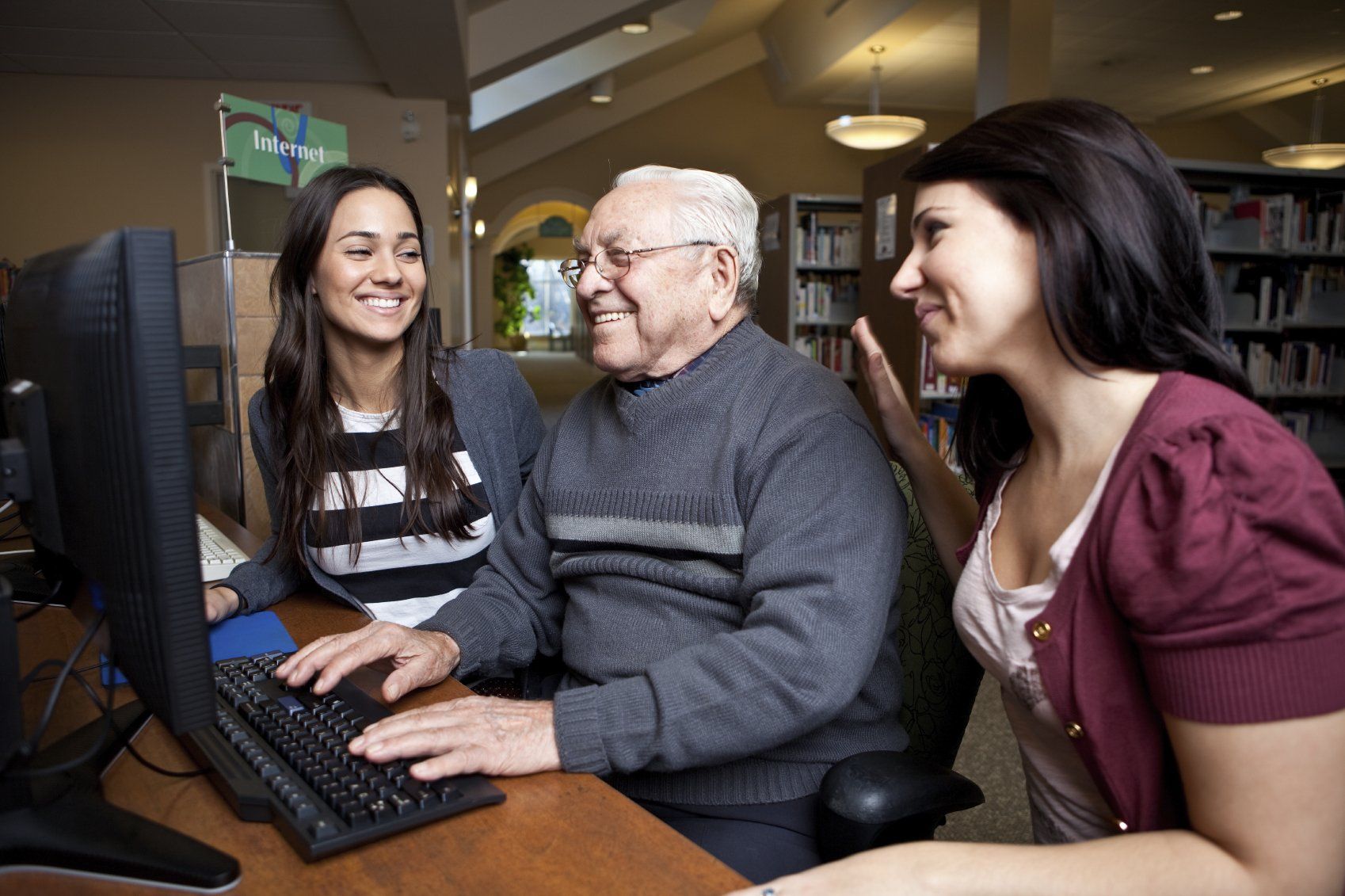 Commit to Lifelong Learning. An older man being taught to use computer by his two daughters.