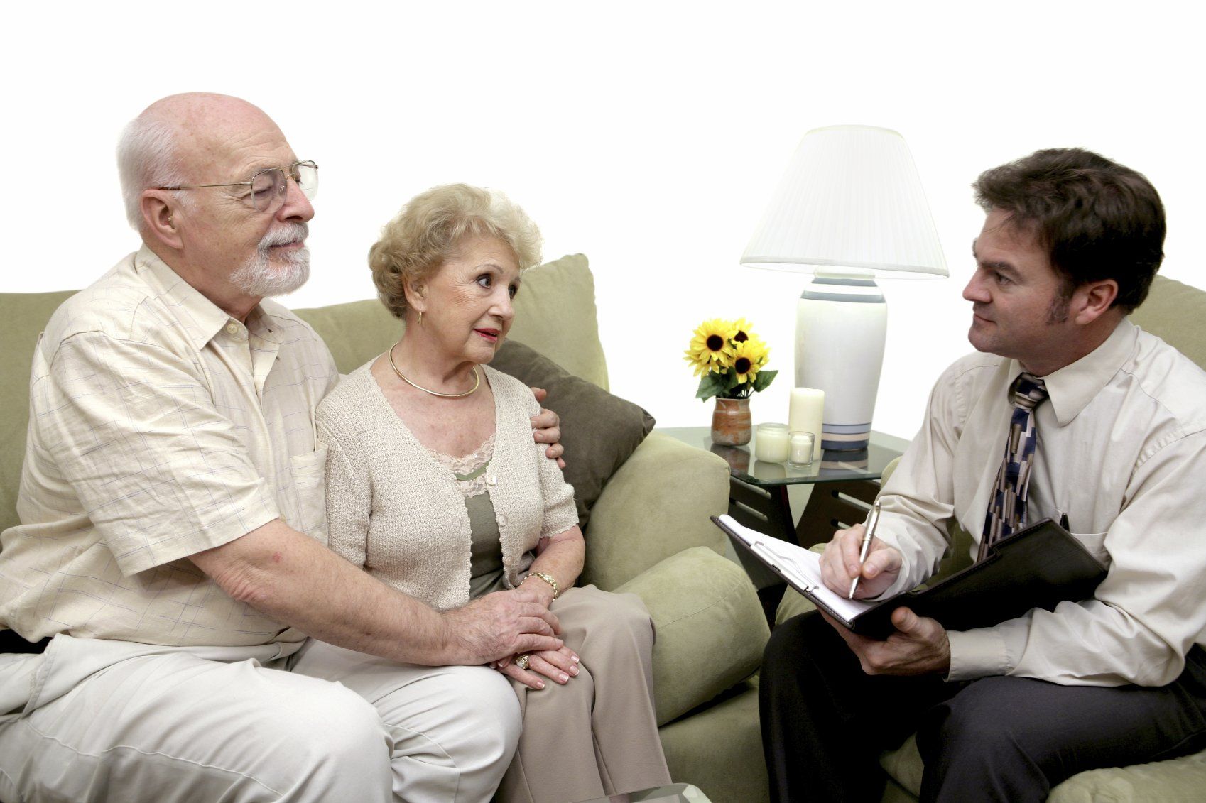 An elderly man and his wife sitting on  a green couch and talking to a counselor.