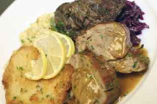 Teller mit Fleisch, Teigtaschen, Rotkohl und Zitronenscheiben.