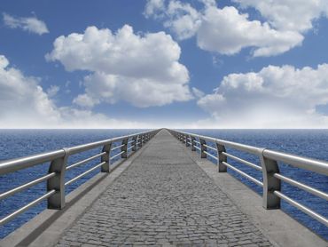 Eine Brücke die über das Meer führt. Rechts und links von der Brücke blaues Wasser über der Brücke der leicht bewölkte blaue Himmel.