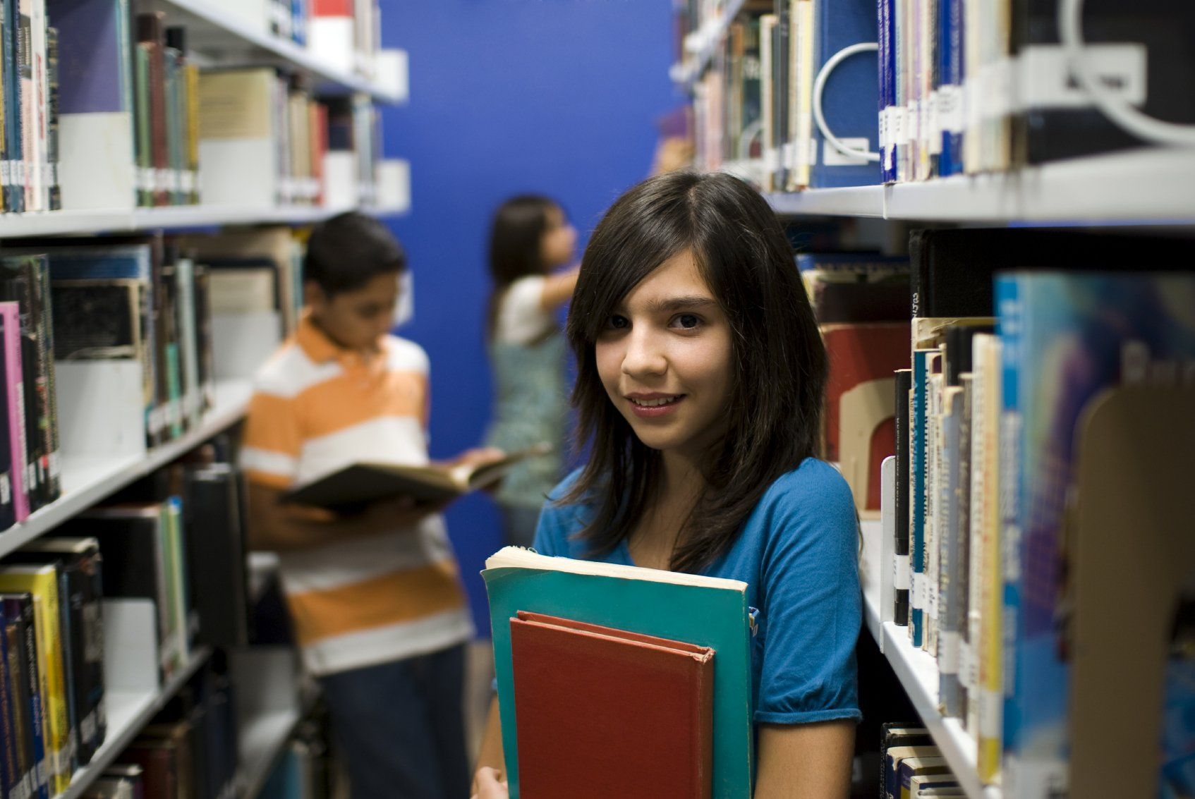 Two young girls and a young boy in library aisle.