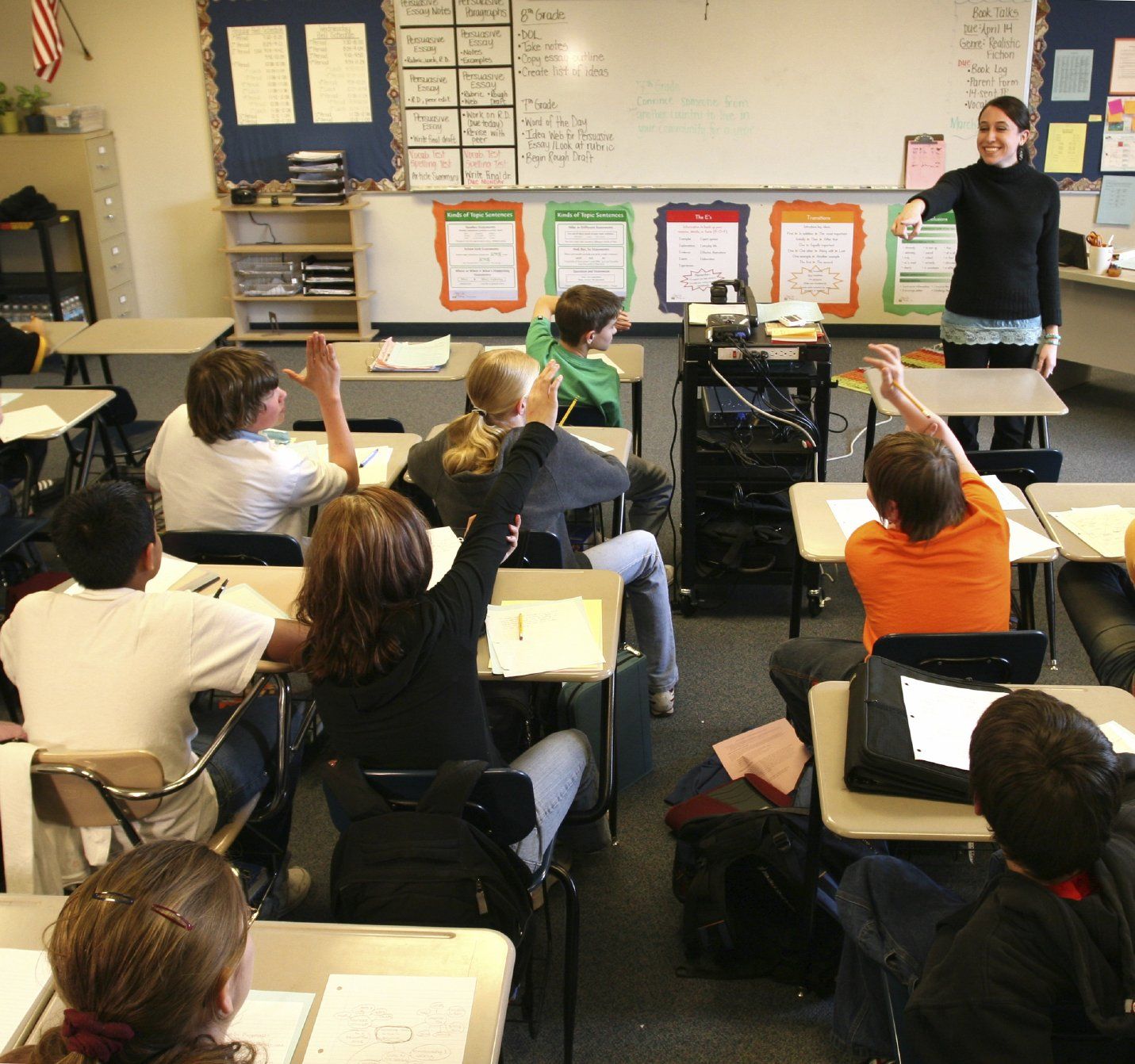 Students in a classroom with their hands raised answering the teacher's questions