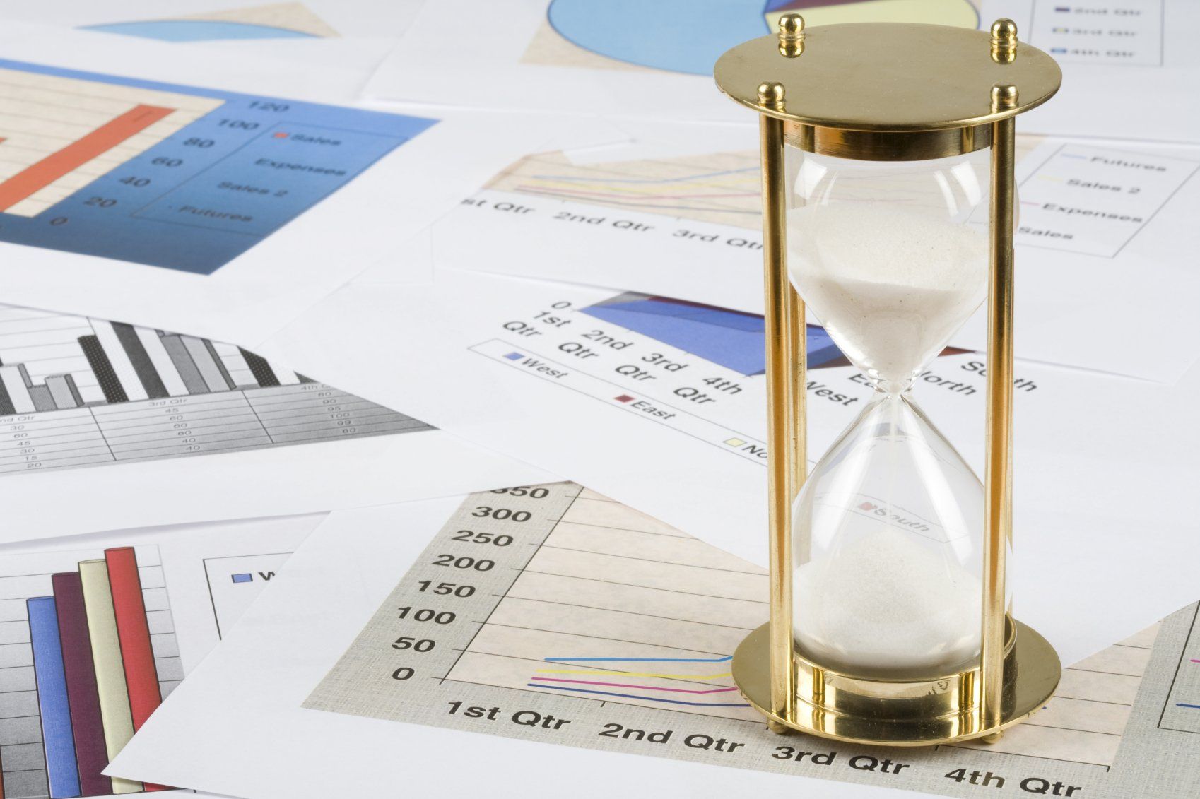A golden hourglass sitting on top of a variety of graph printouts