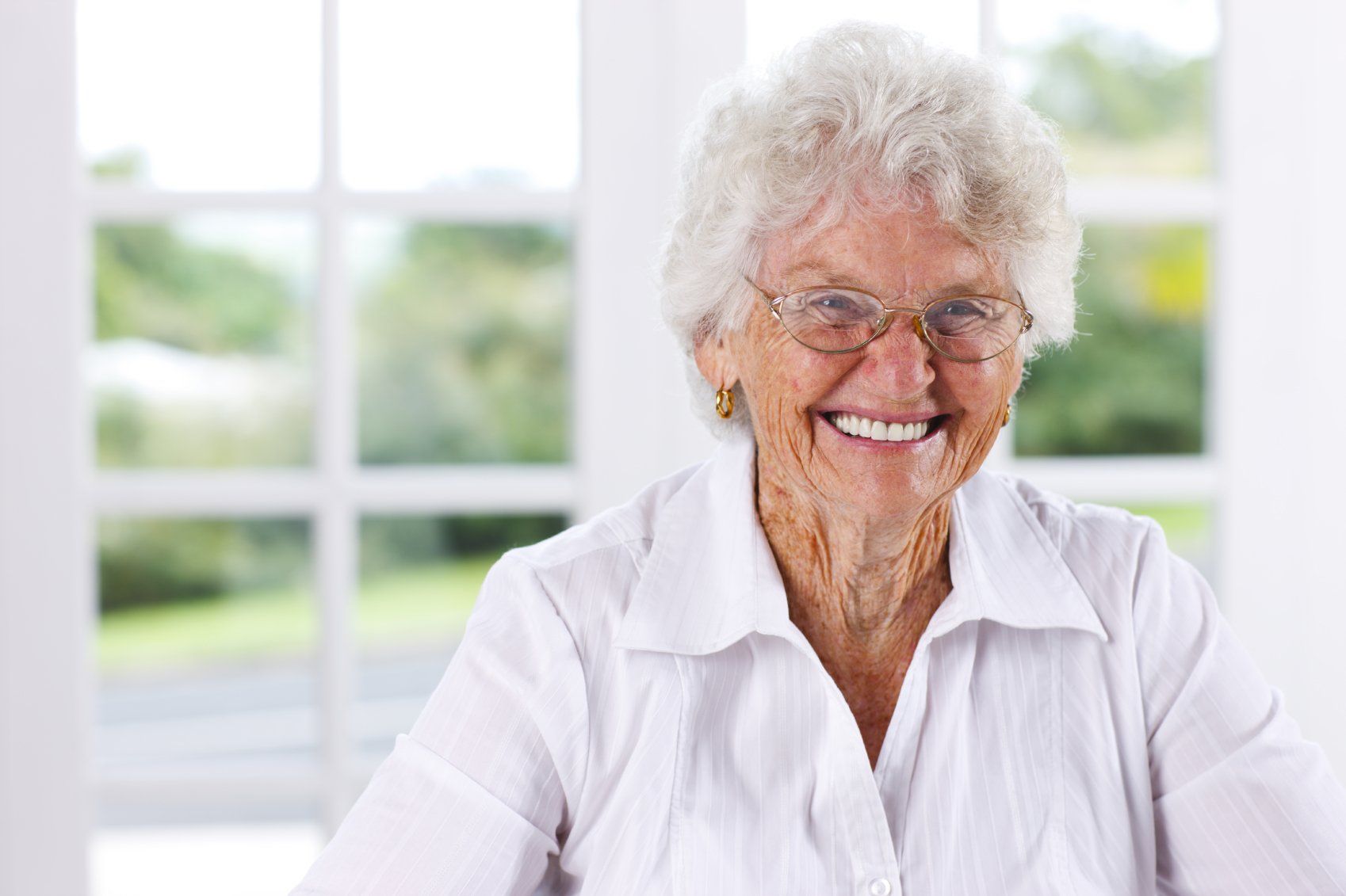 Elderly, grey-haired lady wearing a white shirt and striking a broad smile