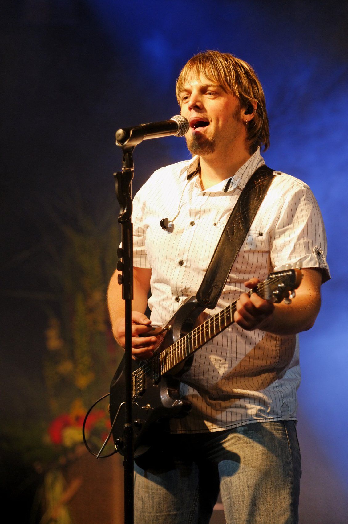 Male musician standing at the microphone, playing a guitar and singing.