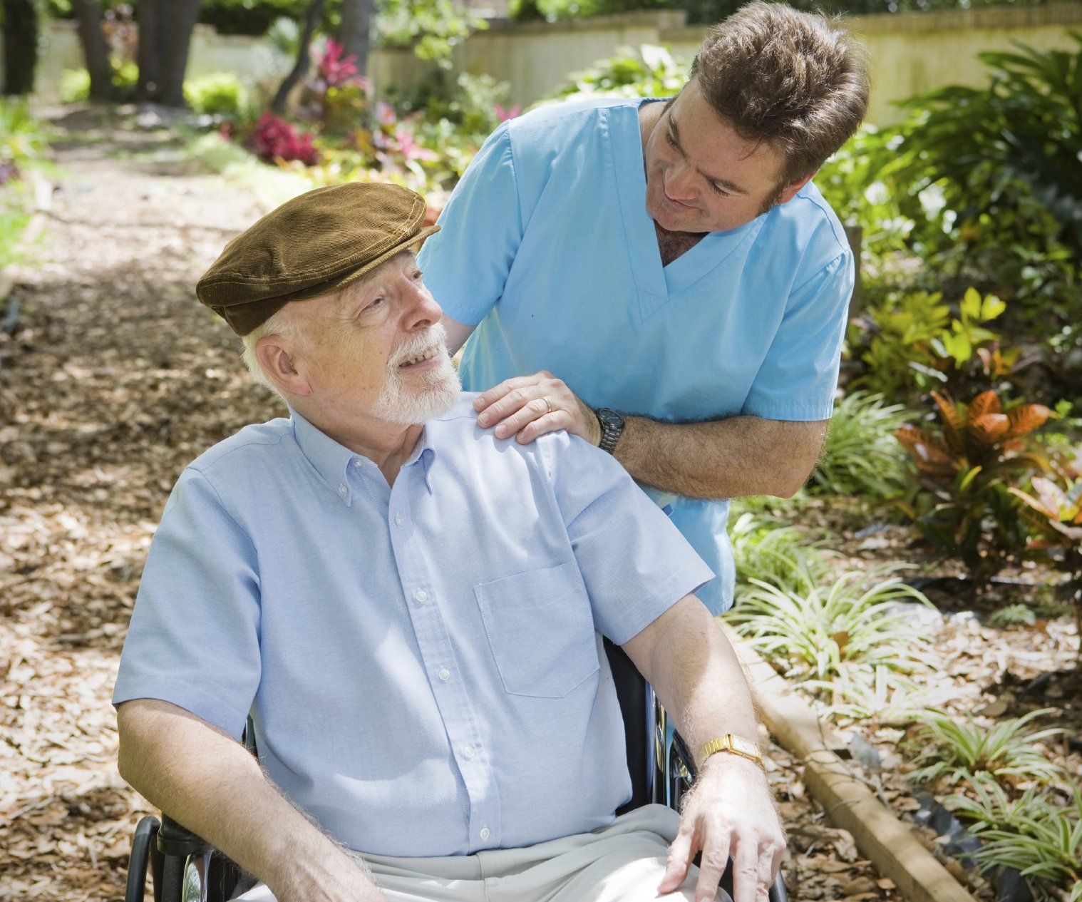 An elderly man in a wheelchair, being assisted by a male nurse.