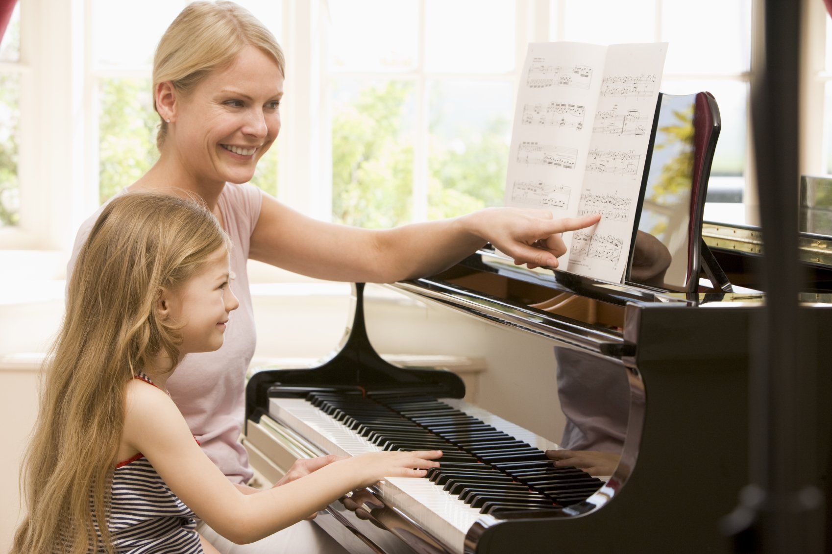 A blonde lady teaching a young, blonde girl at the piano