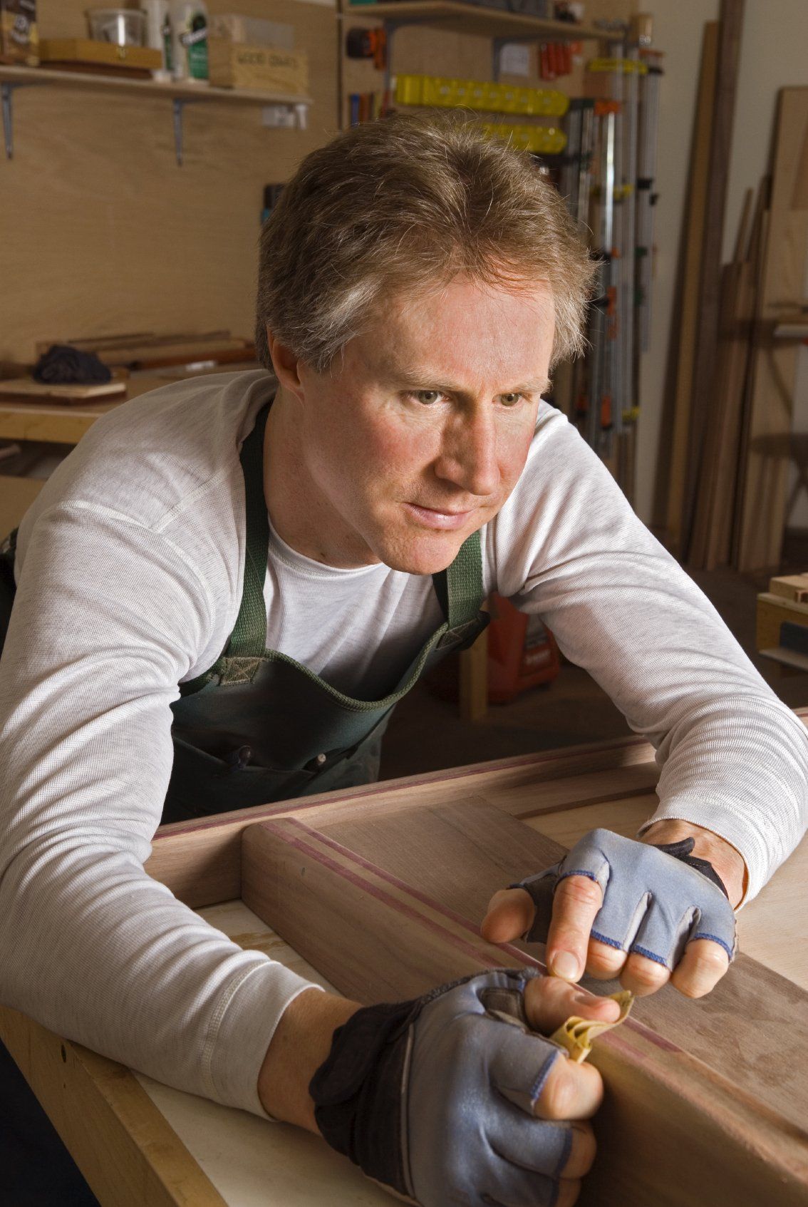 Man in a green apron sanding a piece of woodwork in his shop