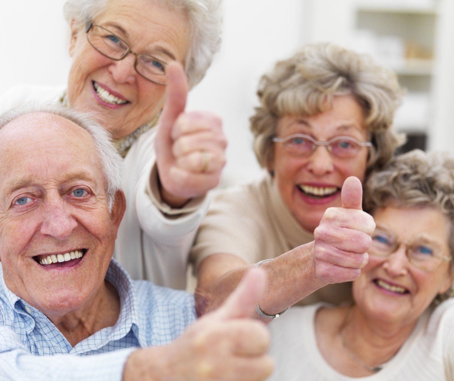 Four senior citizens with broad grins, having a good laugh and giving the thumbs-up sign.
