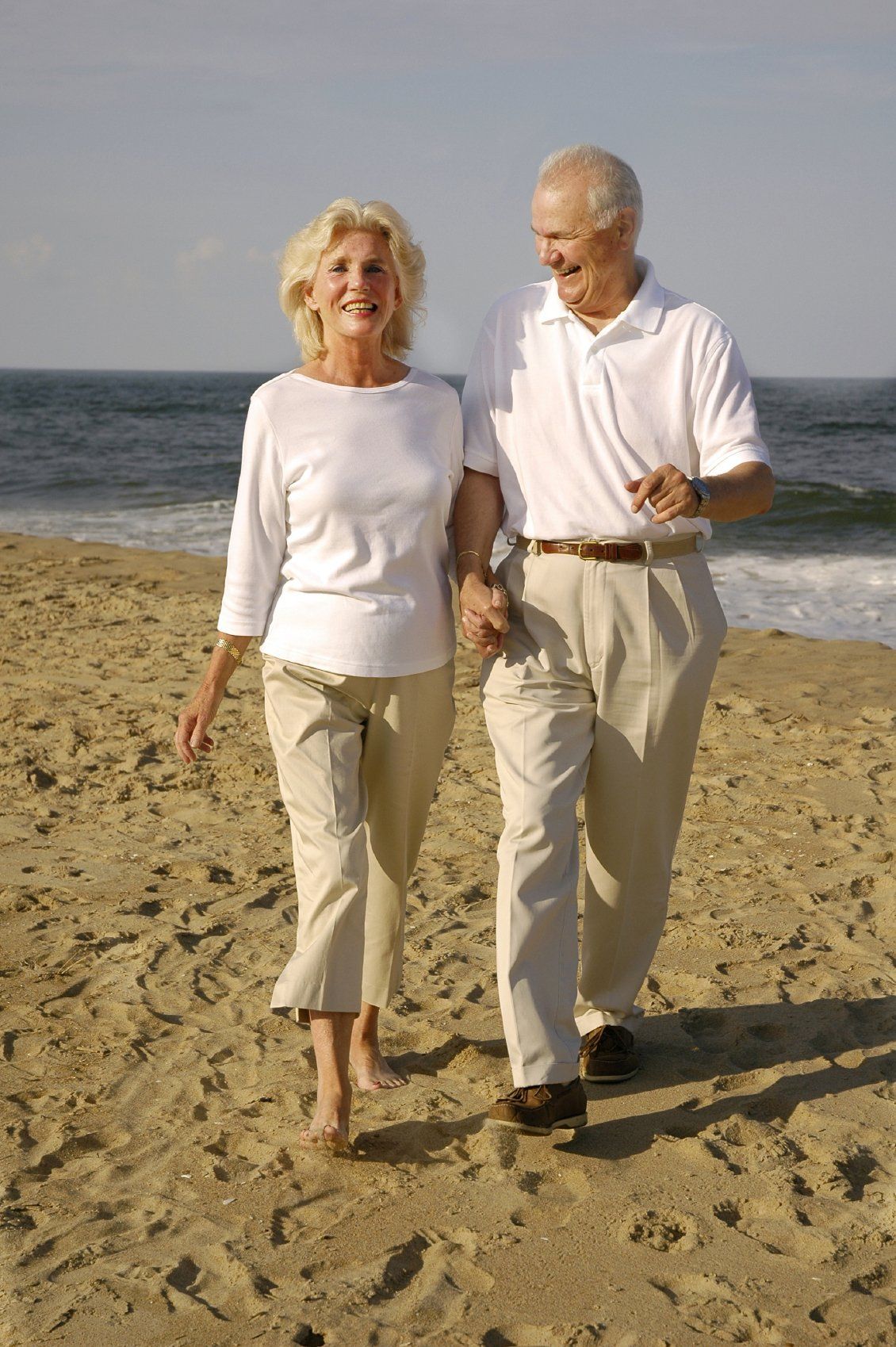 Senior husband and wife walking, hand-in-hand on the beach