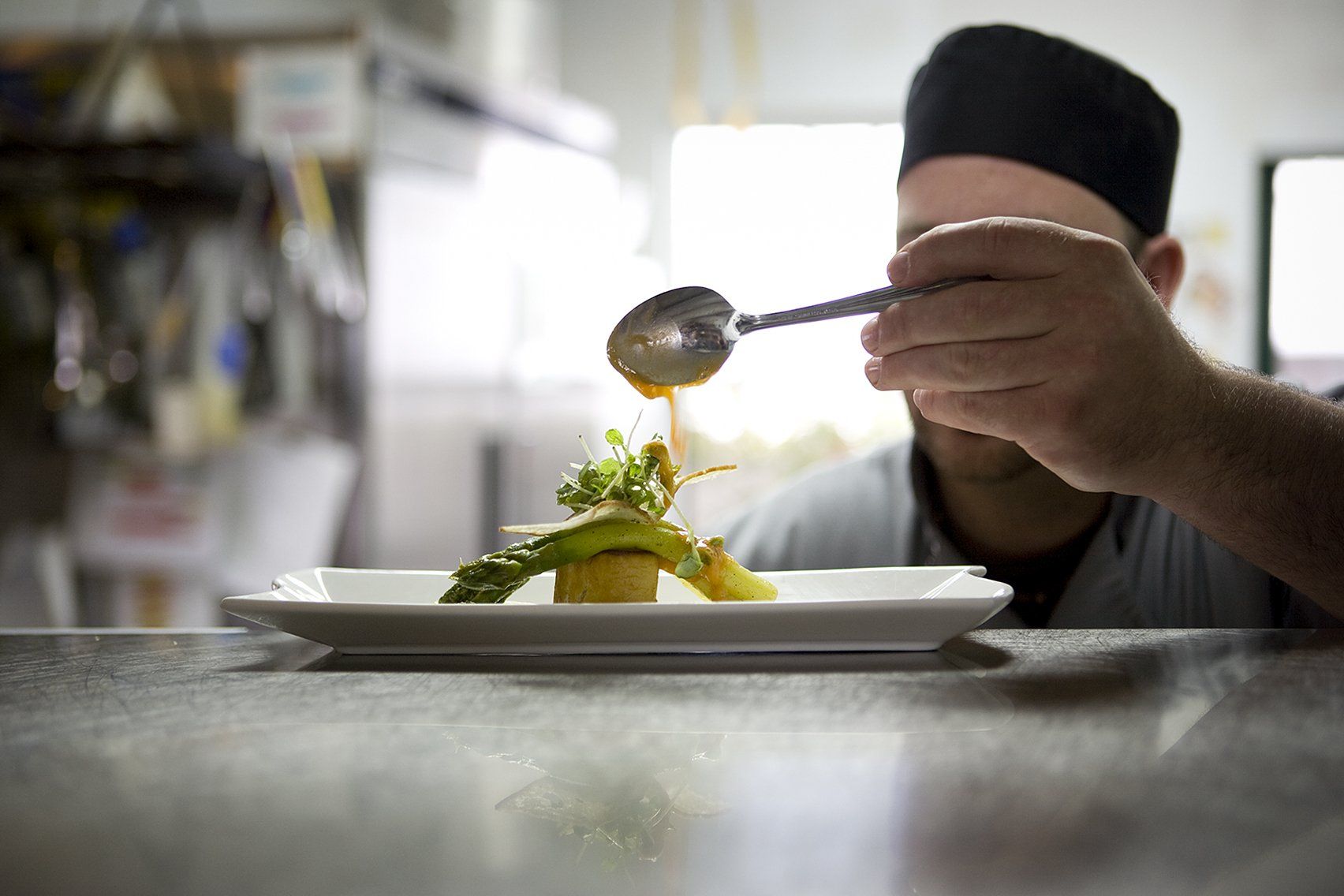 A chef adding a sauce to a vegetable dish before serving to customer.