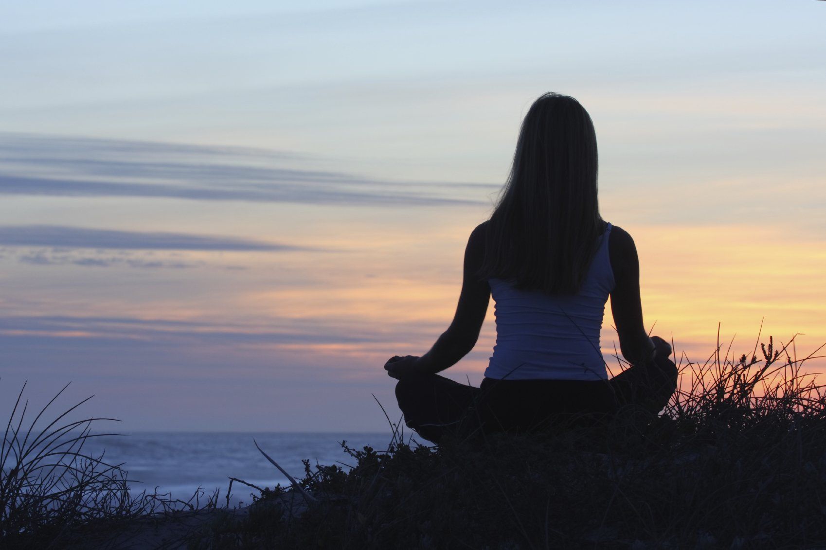 A woman seated in meditation pose with a sunset in the background