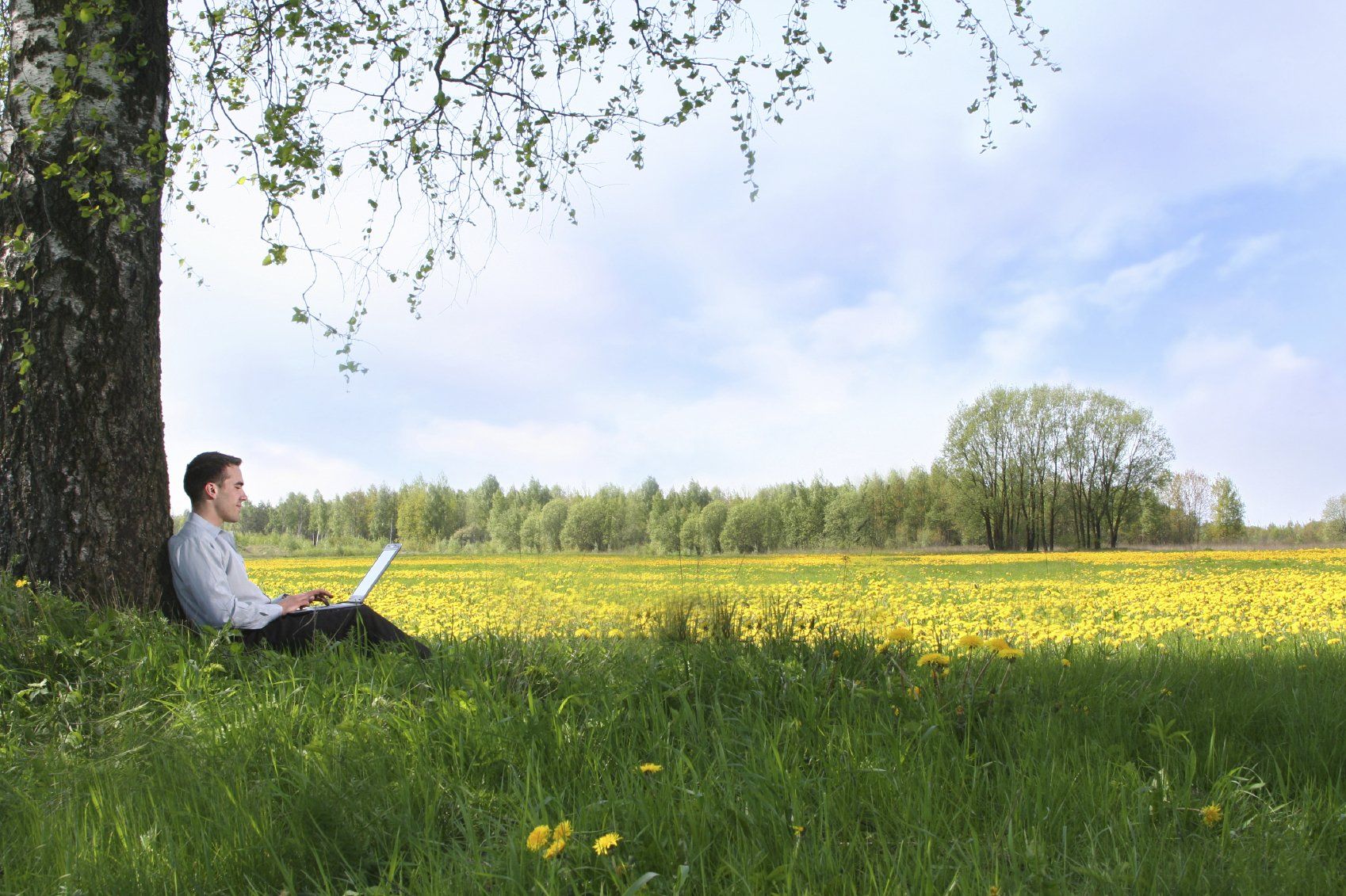 Man with lap top sitting against tree