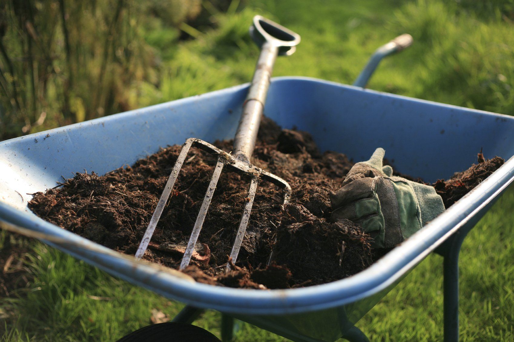 A garden fork and some potting soil sitting in a blue wheel barrow.