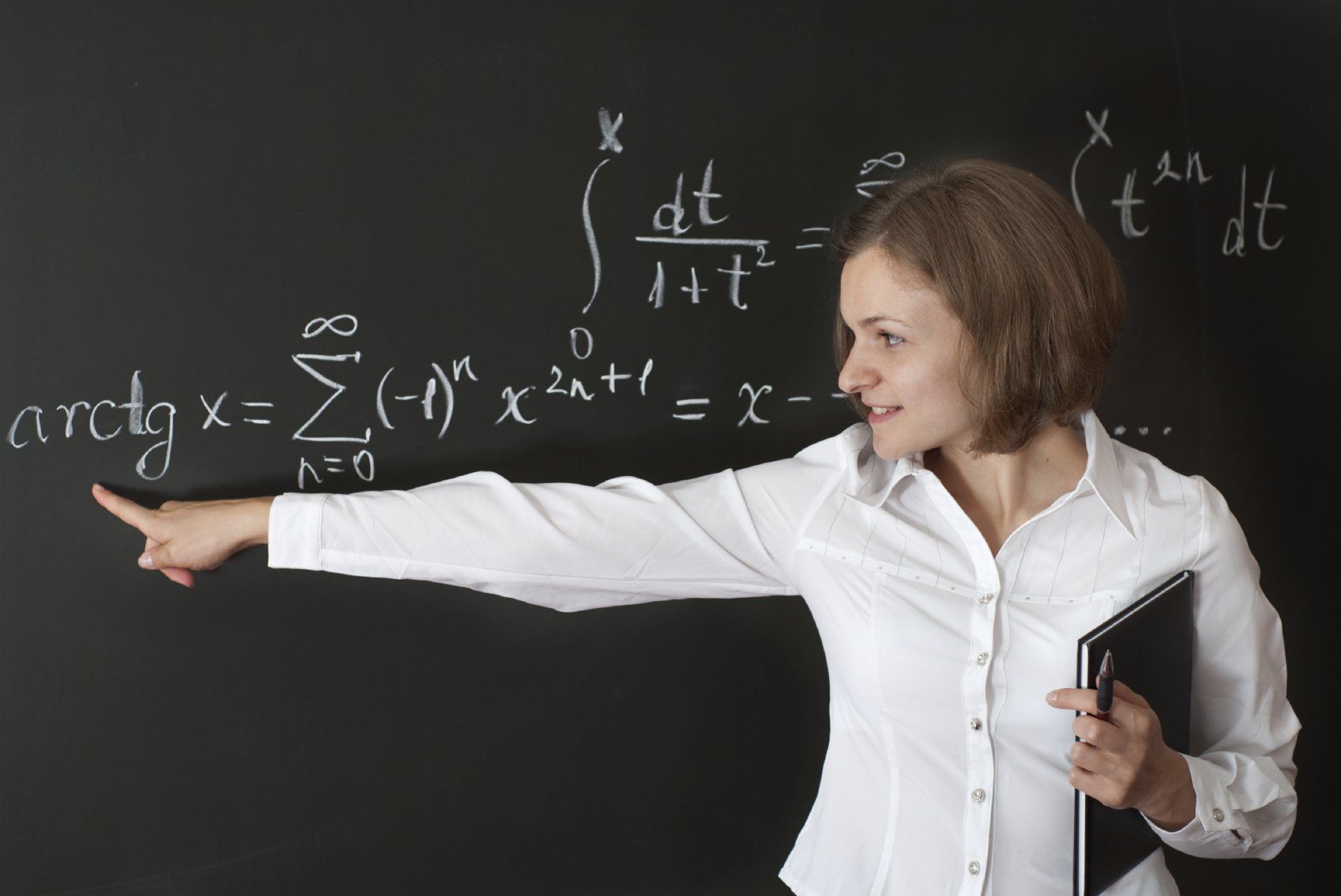 A female teacher in a white blouse explaining a complex mathematical formula on the blackboard.