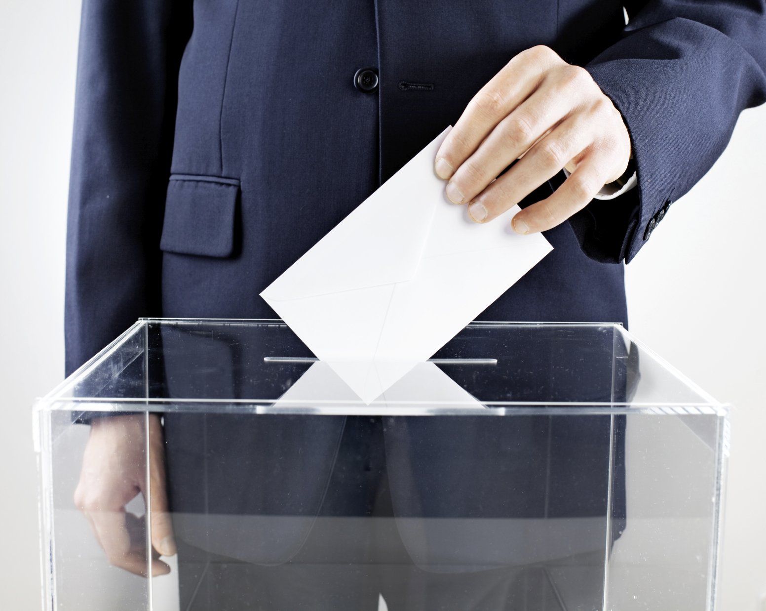 A person in a suit holding an enveloppe or a ballot, putting it into a glass box.