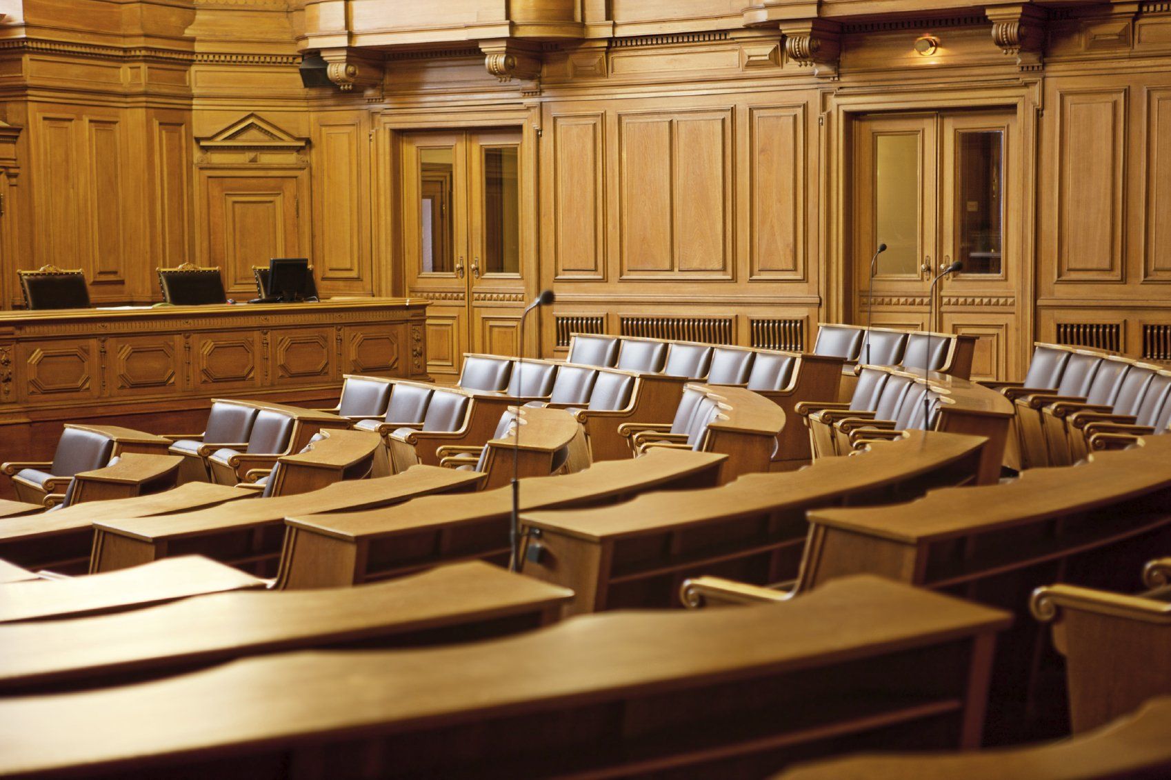Ein leerer, holzgetäfelter Gerichtssaal mit Reihen von Bänken und Schreibtischen, bereit für eine Sitzung zur Italienischen Mediation.