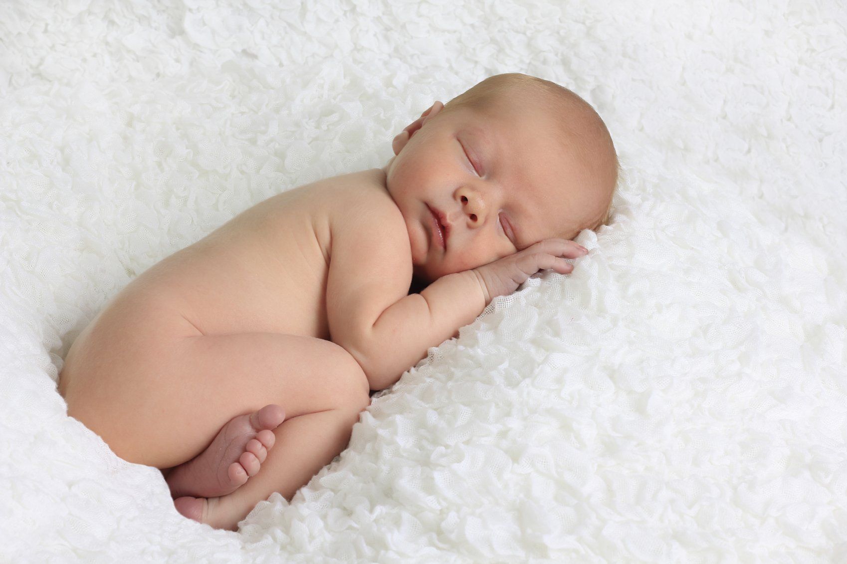 Baby kuschelt sich in eine weiße flauschige Decke