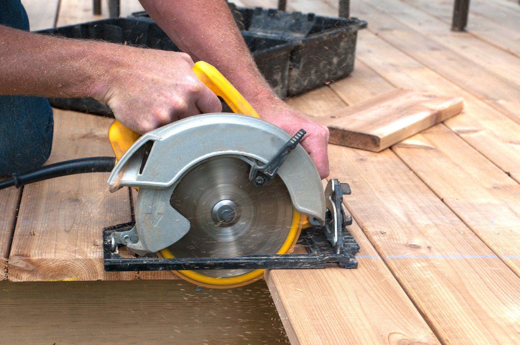 A woodworker cutting a piece of wood with an electric hand saw