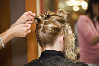 Einer jungen blonden Frau werden die Haare für ein Event hochgesteckt.