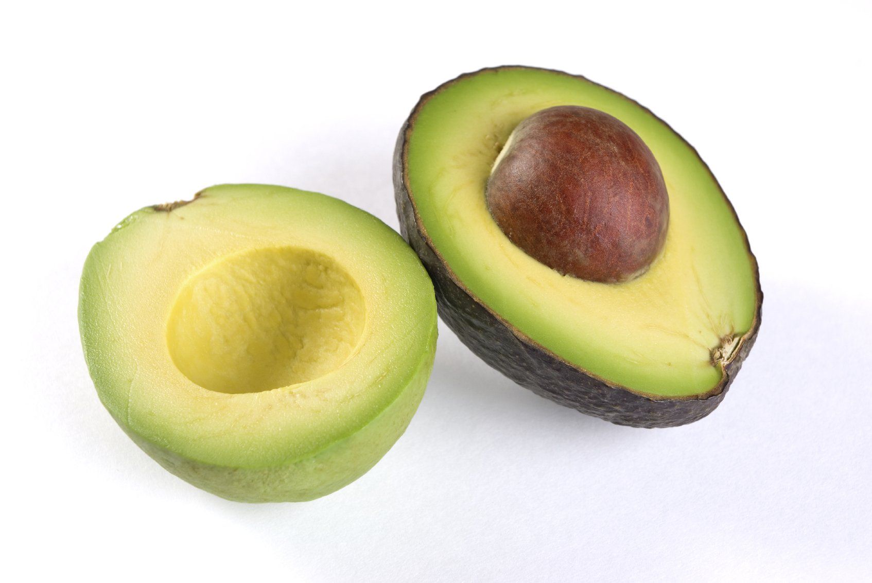 An avocado cut in half with the seed still sitting in one of the halves