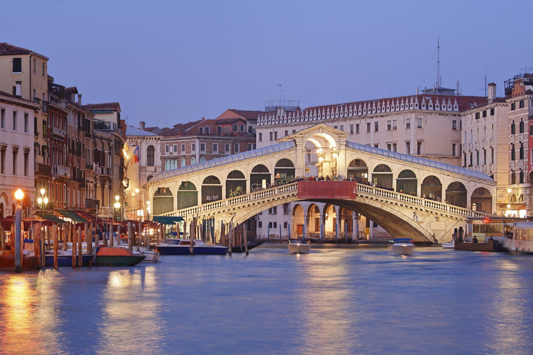 Die in der Dämmerung mit Booten auf dem Canale Grande in Venedig, Italien, beleuchtete Rialtobrücke spiegelt die jüngsten Entwicklungen im italienischen Immobilienrecht wider