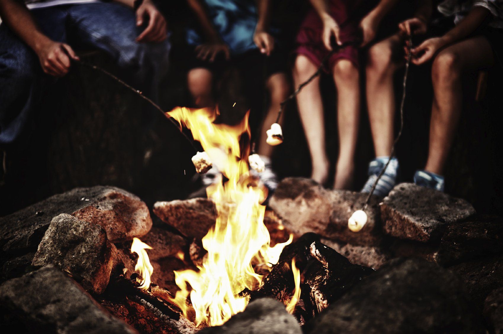 Mikroabenteuer für die Sommerferien Lagerfeuer, Kinder sitzen um ein Feuer