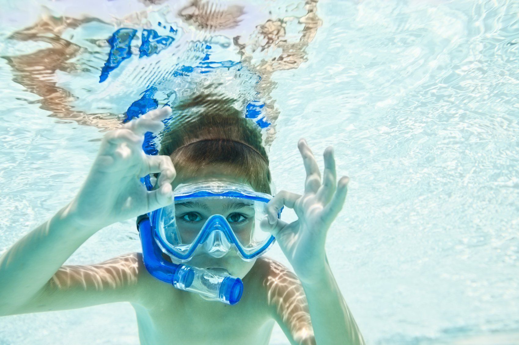 petit garçon qui est sous l'eau et qui fait signe qu'il est content  dans la piscine